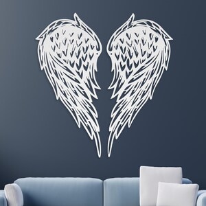 May include: White metal angel wings wall decor, with a detailed design, mounted on a blue wall above a light blue sofa.