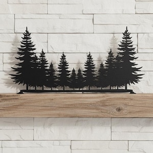 May include: Black metal wall art depicting a forest of pine trees. The silhouette of the trees is mounted on a wooden beam, with a white brick background. The artwork is a decorative piece for home decor.
