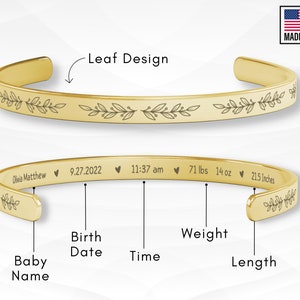 May include: Gold bangle bracelet with a leaf design engraved around the edge. The bracelet is personalized with the baby's name, birth date, time, weight, and length.  The text reads: Olivia Matthew 9.27.2022 11:37 am 71 lbs 14 oz 21.5 Inches