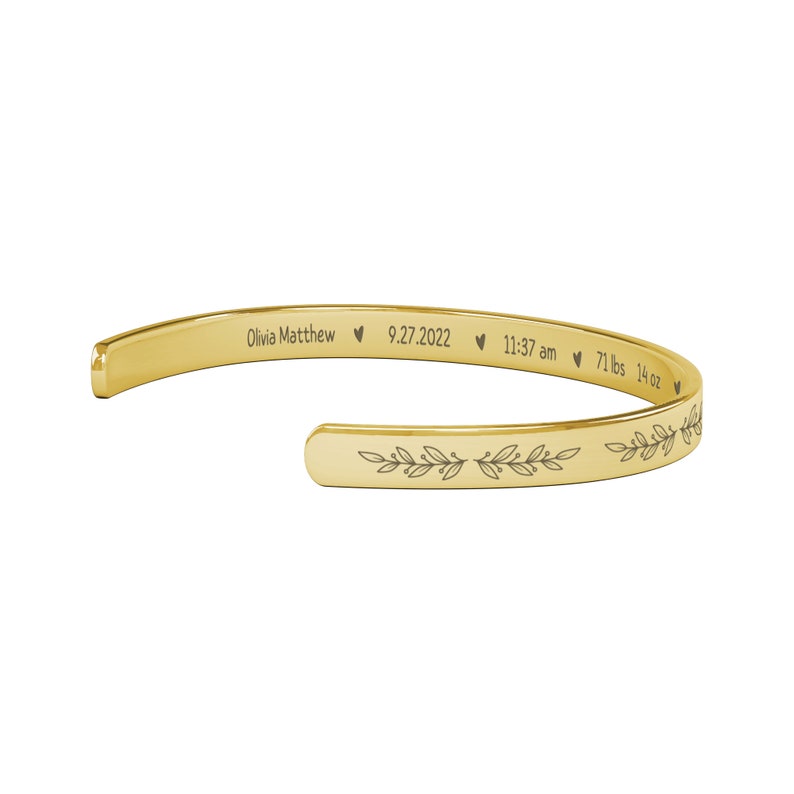 May include: Gold bangle bracelet with an engraved inscription: "Olivia Matthew &hearts; 9.27.2022 &hearts; 11:37 am &hearts; 7 lbs 14 oz" and a leafy design.