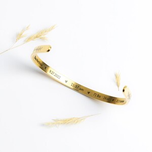 May include: Gold-toned bangle bracelet with an engraved inscription: "Baby Matthew 9.27.2022 &hearts; 11:37 am &hearts; 7 lbs 14 oz &hearts; 21.5 inches".