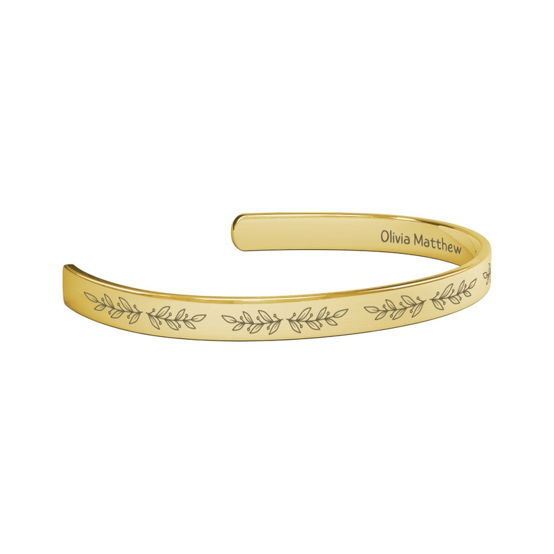 May include: Gold bangle bracelet with an engraved floral design and the name "Olivia Matthew" on the inside.