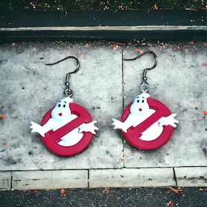 Peut inclure: Une paire de boucles d'oreilles représentant le logo de Ghostbusters. Chaque boucle d'oreille présente un cercle rouge avec une figure de fantôme blanc barrée d'une ligne rouge. Les boucles d'oreilles ont des crochets argentés.