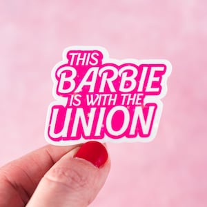 May include: A pink sticker with the text "This Barbie is with the Union" in white letters. The sticker has a glittery background.