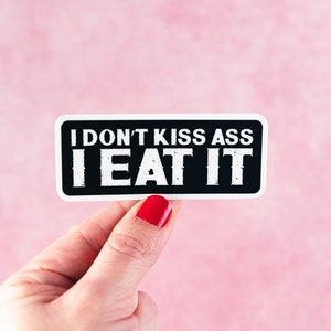 May include: A black and white sticker with the text "I don't kiss ass I eat it" on a pink background.