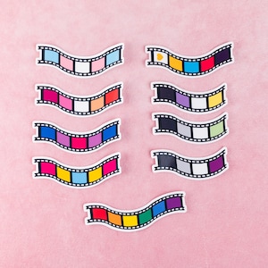 May include: Nine colorful film strips with different color combinations. Each strip has a white border and a black film reel design. The strips are arranged in three rows of three on a pink background.