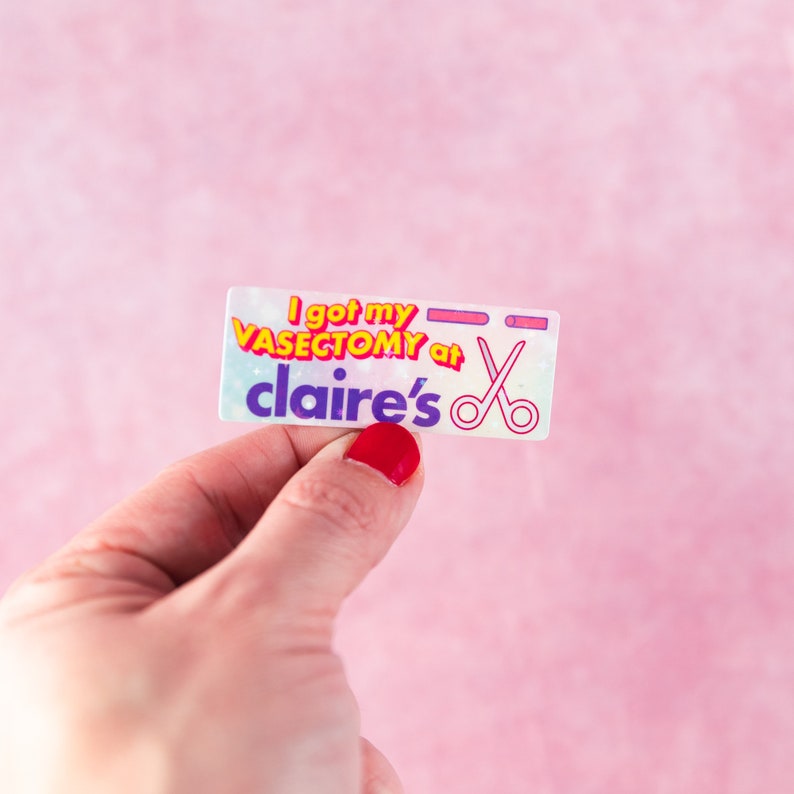 May include: A sticker with a rainbow background and the text "I got my vasectomy at claire's" in purple and yellow letters. A pair of scissors is next to the text.