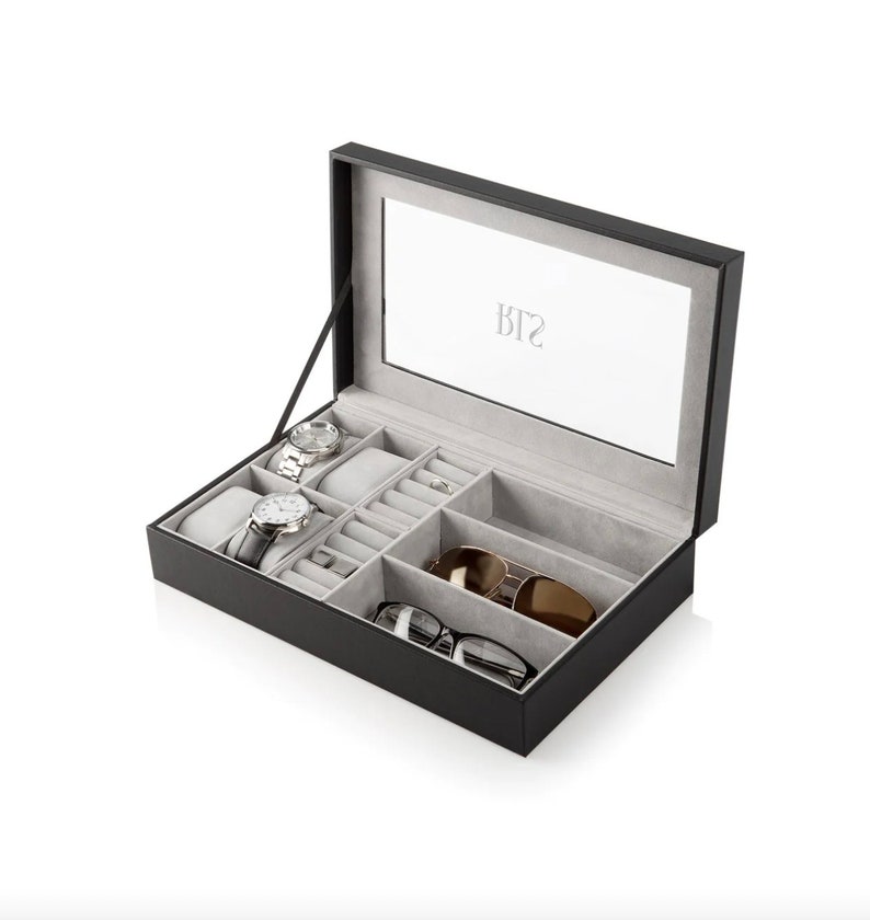 May include: Black leather watch and jewelry box with a mirrored lid. The box has compartments for watches, rings, and sunglasses.