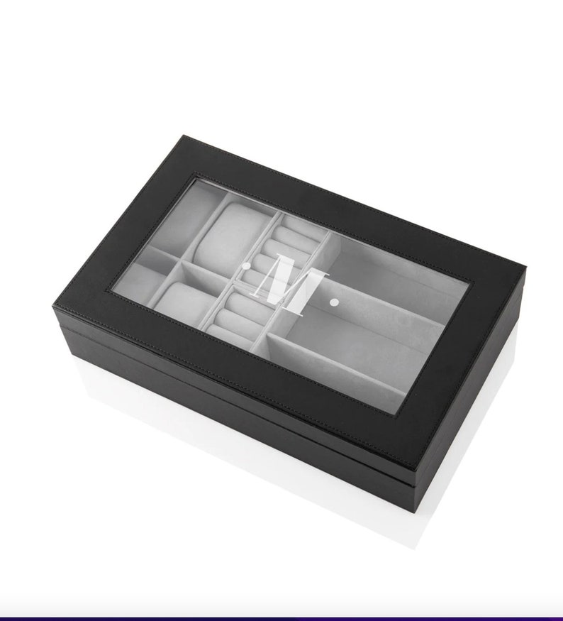 May include: Black leather jewelry box with a clear lid and gray felt lining. The box has a compartment for watches and rings. The box is monogrammed with the initial "M".