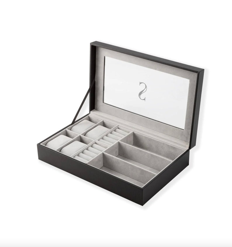 May include: Black leather watch box with a glass top and gray felt lining. The box has multiple compartments for storing watches and rings. The box has an initial "S" engraved on the top.