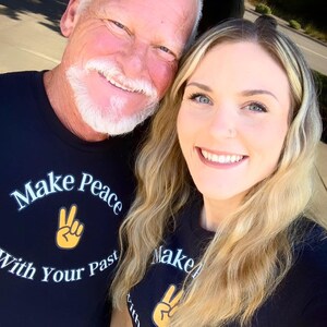 May include: A father and daughter wearing black t-shirts with the text "Make Peace With Your Past" and a peace sign graphic. The shirts are black with white and yellow text and graphics.