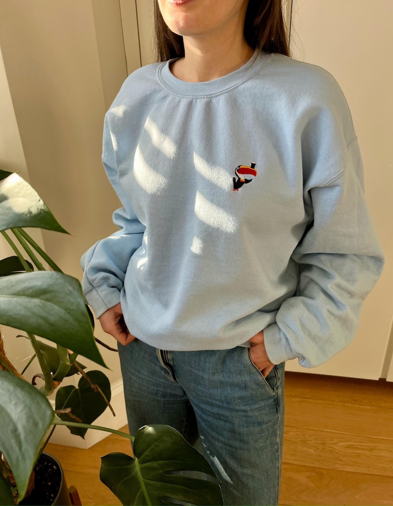 Peut inclure: Un sweat-shirt bleu clair avec un petit toucan brod&eacute; sur la poitrine.