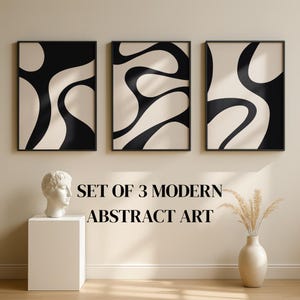May include: A set of three framed modern abstract art prints. Each print has a black and cream wavy design. The artwork is displayed above a white pedestal with a bust and a vase with dried plants.