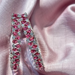 May include: Two silver bangles set with pink pear-shaped stones and clear round stones.