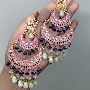 May include: Pink and gold-toned chandelier earrings with a crescent moon design. The earrings feature white, blue, and green beads, and a large pearl drop. The earrings have a floral design at the top.