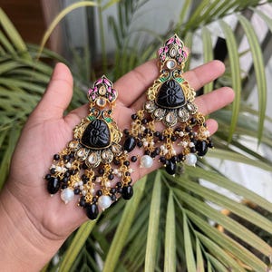 May include: A pair of black and gold earrings with black and white beads. The earrings feature a floral design and a black stone in the centre.