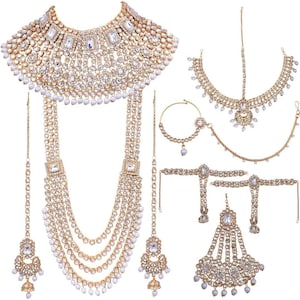 May include: A complete gold-toned bridal jewelry set featuring a statement necklace, long layered necklace, headpiece, nose ring, arm cuffs, and earrings. The set is adorned with clear crystals and white pearls, creating a luxurious and elegant look.