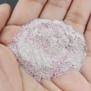 Puede incluir: Primer plano de un montón de arena fina blanca y rosa. La arena es muy fina y tiene un aspecto ligeramente brillante.