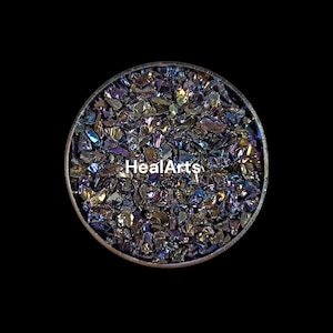 May include: A circular container filled with iridescent, crushed crystals. The crystals display a range of colors including blue, purple, and gold. The text "HealArts" is printed in white across the center of the image.