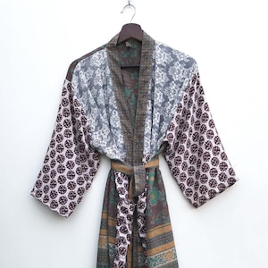 May include: A long, patterned robe with a belt, hanging against a white background. The robe features a mix of patterns, including floral and geometric designs in shades of pink, gray, green, and gold. The robe is made of a lightweight fabric.