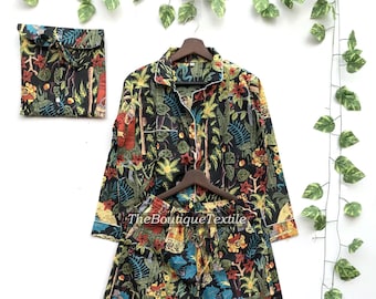 May include: A black pajama set with a colorful floral and human figure print. The set includes a long-sleeved shirt and pants. The shirt has a button-up front and a collar. The pants have an elastic waistband.