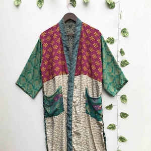 Peut inclure: Une robe à manches longues présentant un motif patchwork avec une section supérieure magenta à motifs floraux jaunes, une section inférieure crème à petites marques sombres, des manches vertes à motifs dorés et deux poches vertes à motifs floraux.