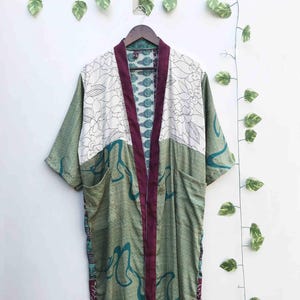 May include: A long-sleeved kimono-style robe featuring a mix of patterns and colors. The upper section has a white floral print, while the lower body is sage green with teal abstract lines. It includes a solid dark maroon trim along the front opening.