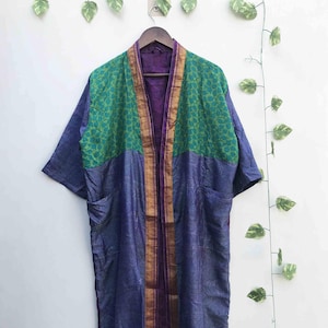 May include: A long-sleeved kimono-style robe featuring a deep purple base with a contrasting green upper panel adorned with a leaf pattern. The garment includes a prominent gold-toned border along the front opening and two side pockets.