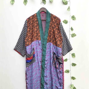 May include: A long-sleeved kimono-style robe featuring a patchwork design of various fabrics. The garment includes panels of orange floral print, black and white geometric patterns, and purple paisley motifs, finished with a solid teal trim.