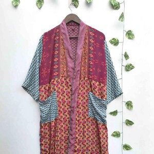 May include: A long-sleeved kimono-style robe featuring a patchwork design with various patterns in shades of magenta, yellow, and teal. The garment has a solid mauve collar, two front pockets, and a repeating geometric print throughout the body.