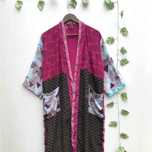 May include: A long-sleeved kimono-style robe featuring a patchwork design with magenta paisley patterns on the upper section and dark brown paisley patterns on the lower section. The sleeves and pockets display a light blue and white geometric print.