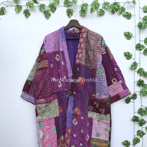 Puede incluir: Un kimono acolchado de patchwork morado y rosa con un patrón floral. El kimono tiene una silueta larga y fluida y es perfecto para superponer sobre un vestido o unos vaqueros.