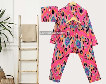 May include: Pink and black pajama set with an ikat print. The set includes a long-sleeved shirt with a button-up front and matching pants with an elastic waistband.