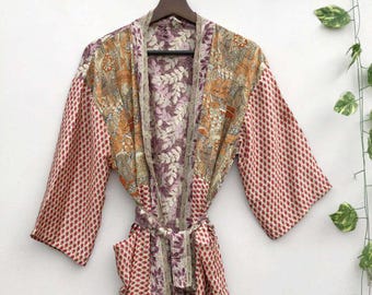 Może przedstawiać: Kolorowe kimono w wzory. Szlafrok ma mieszankę kwiatowych i geometrycznych wzorów w odcieniach czerwieni, pomarańczy, fioletu i beżu. Ma szerokie rękawy i pasujący pasek.