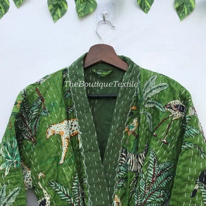 May include: Green quilted robe with a jungle print featuring zebras, leopards, birds, and palm trees. The robe has a V-neck and is made of cotton. The text "TheBoutiqueTextile" is printed on the robe.