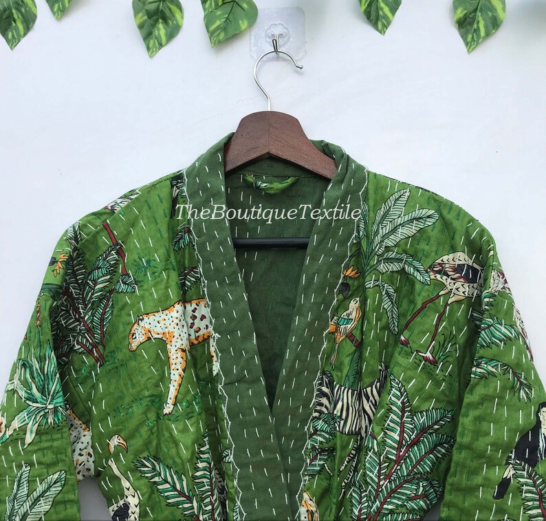May include: Green quilted robe with a jungle print featuring zebras, leopards, birds, and palm trees. The robe has a V-neck and is made of cotton. The text "TheBoutiqueTextile" is printed on the robe.