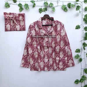 May include: A pink pajama top with a white cat print. The top has a button-up front and a collar.