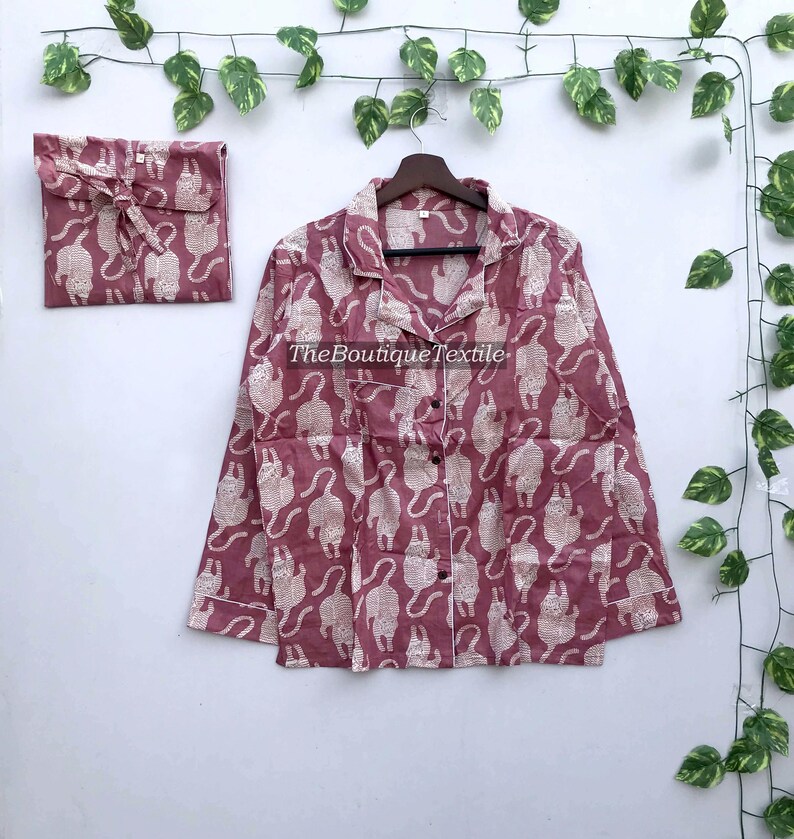 May include: A pink pajama top with a white cat print. The top has a button-up front and a collar.