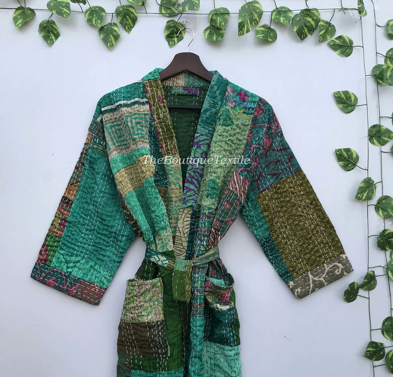 May include: A green quilted robe with a patchwork design featuring various floral and geometric patterns. The robe has a tie belt and long sleeves.