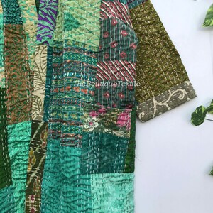 May include: A green patchwork kantha quilt jacket with a floral print. The jacket has a long sleeve and a button closure. The fabric is quilted with white thread.