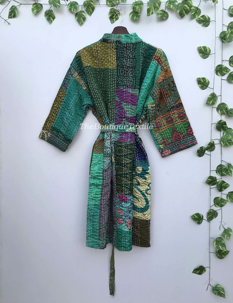 May include: A green, blue, and purple patchwork quilted robe with a tie belt. The robe has a variety of floral and geometric patterns. The text "TheBoutiqueTextile" is visible on the robe.
