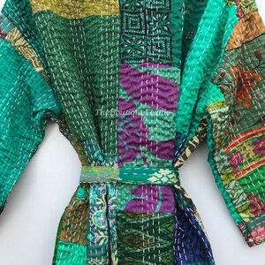 May include: A green, purple, and brown patchwork robe with a white embroidered design. The robe has a sash tie and long sleeves.
