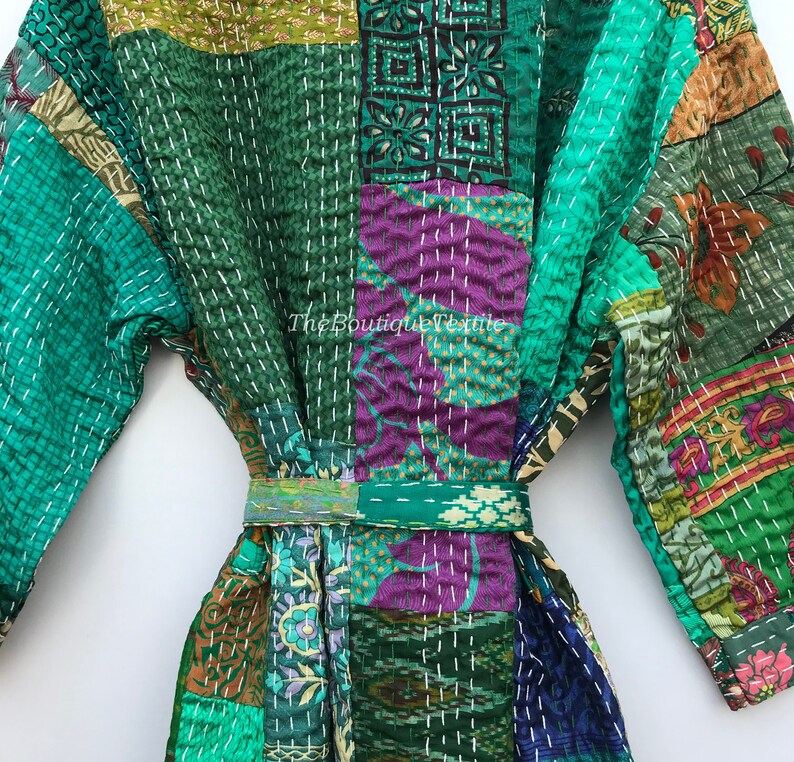 May include: A green, purple, and brown patchwork robe with a white embroidered design. The robe has a sash tie and long sleeves.