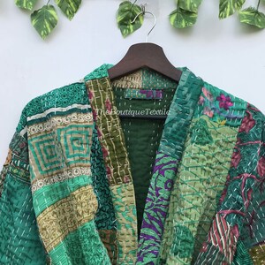 May include: A green kantha quilt jacket with a patchwork design. The jacket has a V-neck and is made of recycled saris. The Boutique Textile label is visible on the front of the jacket.