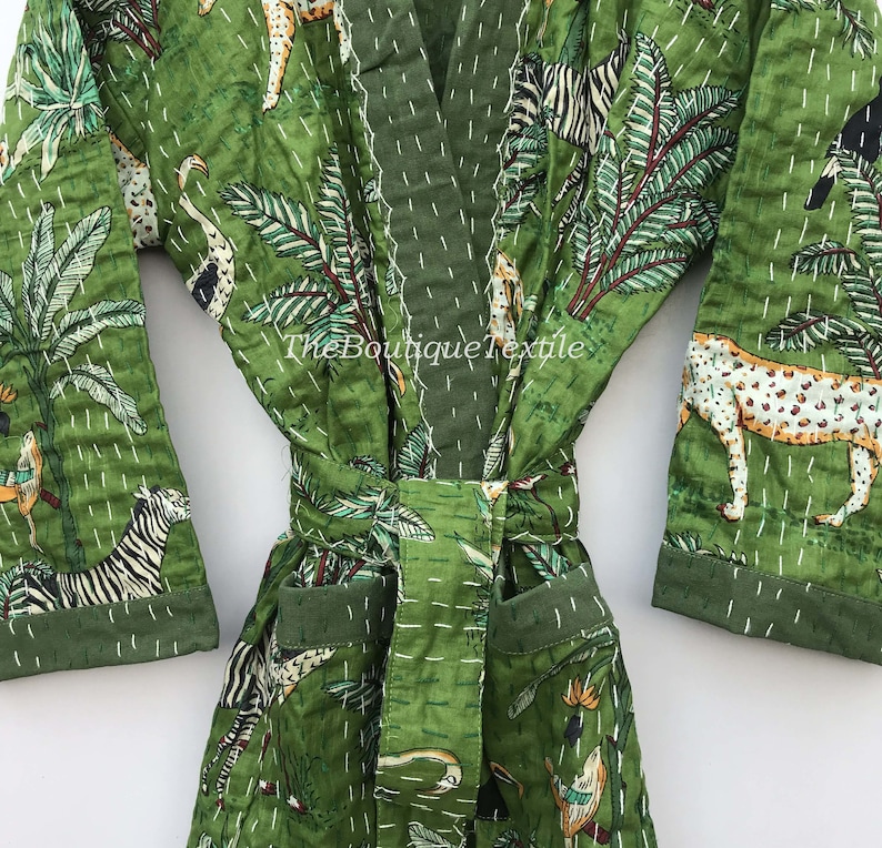 May include: Green cotton robe with a jungle print featuring zebras, leopards, and palm trees. The robe has a tie belt and pockets. The text "TheBoutiqueTextile" is printed on the robe.