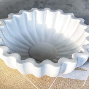 May include: White ceramic bowl with a scalloped edge. The bowl is shaped like a flower and has a smooth, glossy finish.