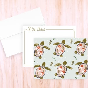 May include: Stationery set featuring a patterned design of sea turtles with floral details in pink, white, and orange on a light blue background. Includes a matching envelope and a card with the name "Mrs. Baca" in script.