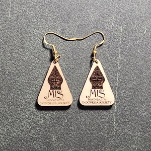 Puede incluir: Un par de pendientes de madera con forma triangular. Los pendientes están grabados con el texto "MIS Minnesota Indonesia Society".
