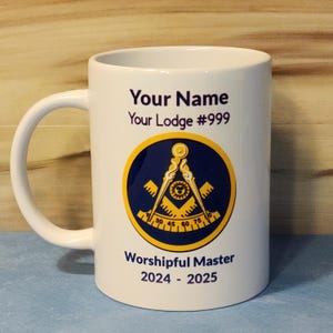 Może przedstawiać: Biały kubek ceramiczny z niebieskim i złotym symbolem masońskim, tekstem "Your Name", "Your Lodge #999", "Worshipful Master" i "2024 - 2025".