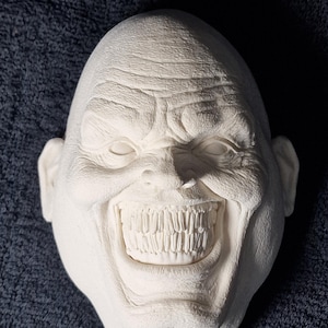 Puede incluir: Una escultura de yeso blanco de una cara con una amplia sonrisa de dientes. La cara es inexpresiva, pero la sonrisa es inquietante.